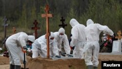 FILE - Grave diggers wearing protective gear bury a presumed victim of the coronavirus disease COVID-19, in a special section of a cemetery on the outskirts of Saint Petersburg, Russia, May 13, 2020. 