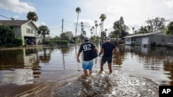 Thomas Chaves, left, and Vinny Almeida walk through floodwaters from Hurricane Helene in an attempt to reach Chaves's mother's house in St. Petersburg, Florida, Sept. 27, 2024.