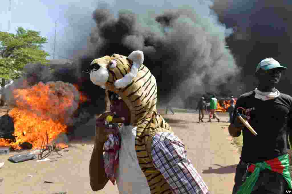 Waandamanaji wasimama nje ya jengo la bunge linapowaka moto pamoja na magari na hati zilizokuwa nje ya jengo, mjini Ouagadougou, Burkina Faso, Oct. 30, 2014. 