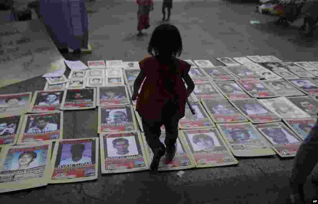 Uma menina filipina caminha por cima de fotos de pessoas desaparecidas durante um ajuntamento de familiares de activistas desaparecidos em Manila, Filipinas, no dia dos Finados.&nbsp; 