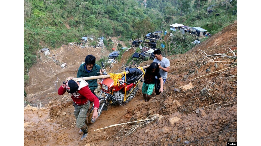 Warga membawa sepeda motor saat berjalan di jalan yang terkikis tanah longsor akibat Topan Mangkhut di kamp pertambangan skala kecil di Itogon, Benguet, Filipina, 19 September 2018. (Foto: Reuters)