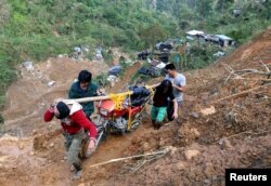 Warga membawa sepeda motor saat berjalan di jalan yang terkikis tanah longsor akibat Topan Mangkhut di kamp pertambangan skala kecil di Itogon, Benguet, Filipina, 19 September 2018. (Foto: Reuters)