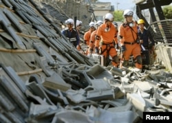 Firefighters walk among collapsed houses caused by an earthquake in Mashiki town, Kumamoto prefecture, southern Japan, in this photo taken by Kyodo, April 15, 2016.