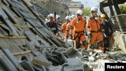FILE - Firefighters walk among collapsed houses caused by an earthquake in Mashiki town, Kumamoto prefecture, southern Japan, April 15, 2016.