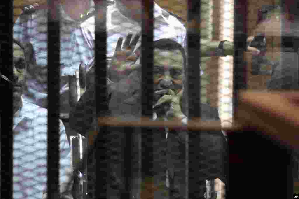 Presiden Mesir terguling Hosni Mubarak melambaikan tangan dalam sidang pengadilan sementara anaknya Gamal (kiri) duduk di sampingnya, di Kairo, 21 Mei 2014.