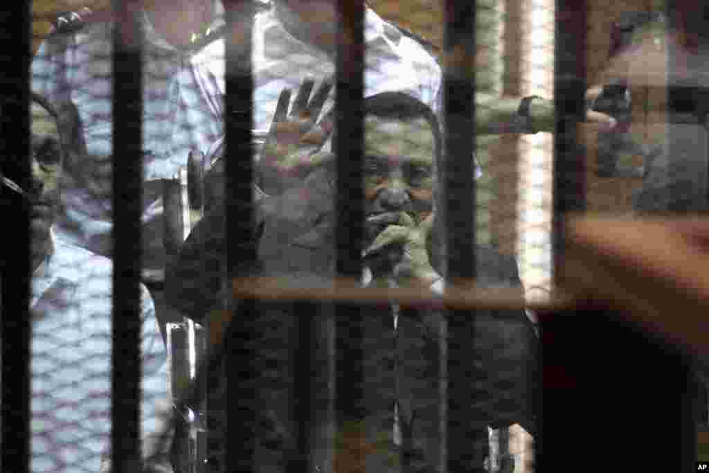 Ousted Egyptian president Hosni Mubarak waves during a court hearing while his son Gamal (left) sits next to him, in Cairo, May 21, 2014.