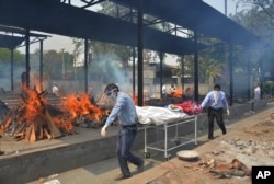 FILE - Relatives carry the body of a person who died of COVID-19 as multiple pyres of other COVID-19 victims burn at a crematorium in New Delhi, India.