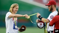 Olympic gold medal swimmer Katie Ledecky, left, hands her medals to Washington Nationals' Bryce Harper, right, to hold before she threw out the ceremonial first pitch before a baseball game between the Baltimore Orioles and the Washington Nationals, Aug. 24, 2016, in Washington, D.C.