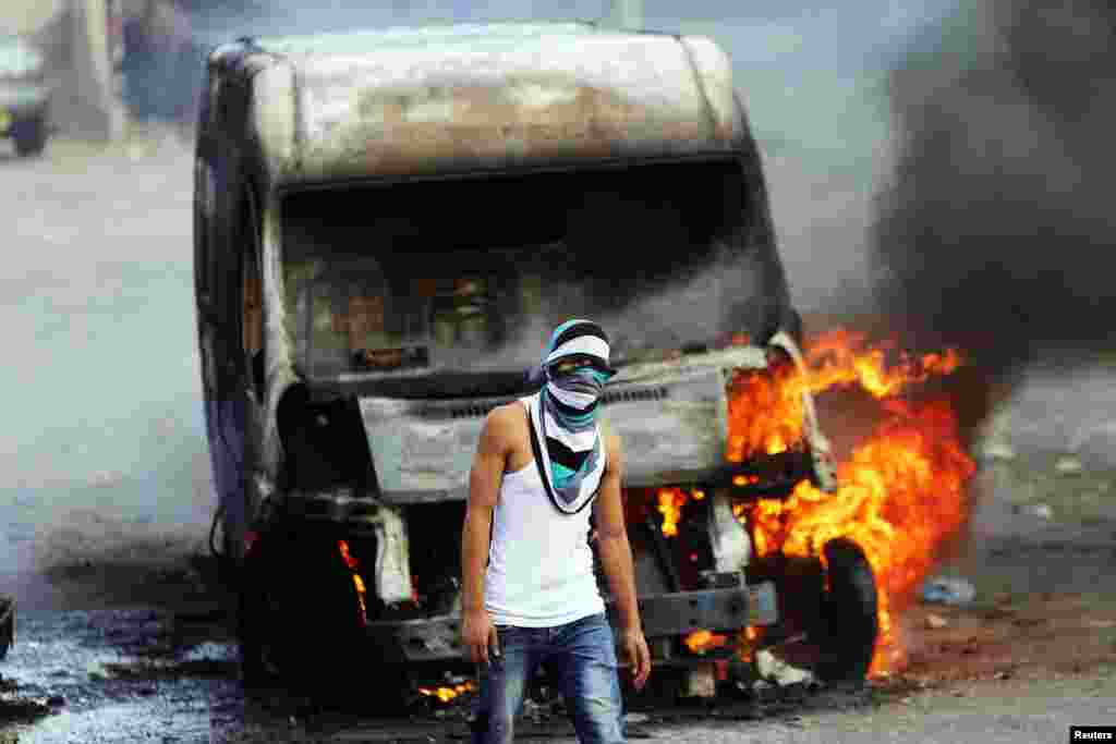 A Palestinian protester stands in front of a car owned by an Israeli. The car was set on fire by the protesters during clashes with Israeli security forces in east Jerusalem, Oct. 30, 2014. 