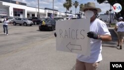 Un voluntario sostiene un cartel de "Raíces Venezolanas" en el punto de entrega de comida para los más necesitados de Miami. 