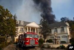 A fire truck is parked outside a mansion as smoke from a wildfire rises behind the property Wednesday, Dec. 6, 2017, in the Bel-Air neighborhood of Los Angeles.