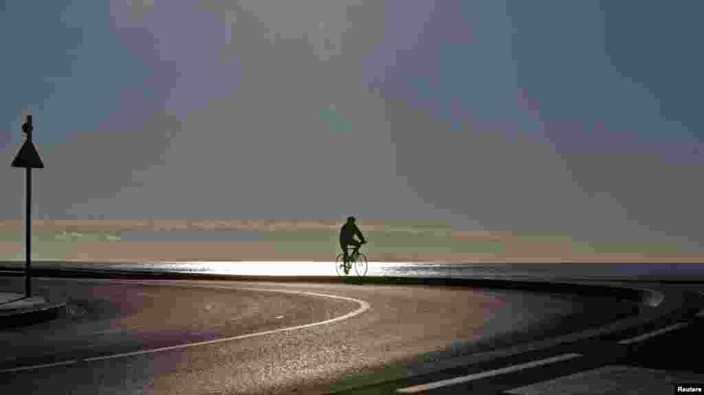 Một người đàn ông đi xe đạp trên đường quanh bãi biển vào một ngày mùa đông có nắng ở Nice, Pháp.