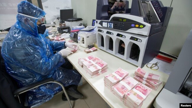 山西省太原市一名银行工作人员身穿雨衣戴着护眼镜和口罩点数人民币。（2020年2月24日）