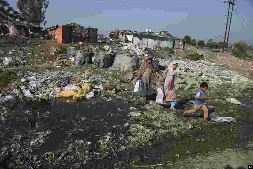 Warga berjalan melewati genangan air yang terkontaminasi polutan industri, di antara permukiman kumuh, di Jammu, India.
