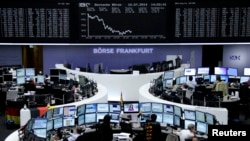 Traders are seen at their desks in front of the DAX board at the Frankfurt stock exchange, Germany, July 10, 2014. 