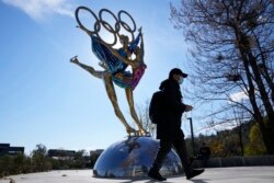 Seorang pengunjung Taman Shougang berjalan melewati patung untuk Olimpiade Musim Dingin Beijing di Beijing, China, Selasa, 9 November 2021. (Foto: AP)