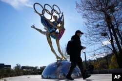 Seorang pengunjung Taman Shougang berjalan melewati patung untuk Olimpiade Musim Dingin Beijing di Beijing, China, Selasa, 9 November 2021. (Foto: AP)