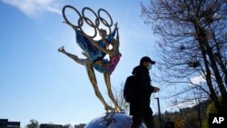 Seorang pengunjung berjalan melewati patung untuk Olimpiade Musim Dingin Beijing di Taman Shougang, Beijing, China, Selasa, 9 November 2021. (AP Photo/Ng Han Guan)