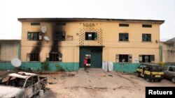 FILE - A man stands in front of the gate of a Nigerian Correctional Services facility that was attacked by gunmen, with large numbers of inmates set freed afterwards, in Imo State, Nigeria April 5, 2021.