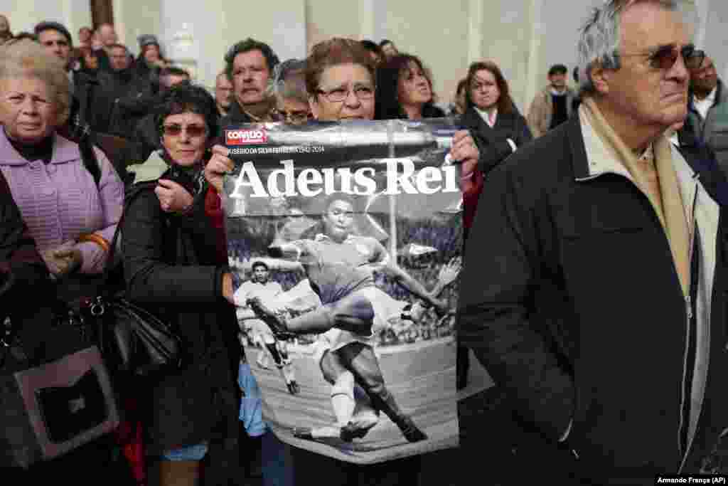 Uma mulher segura um poster em honra a Eusébio, o &quot;rei&quot;, nos Passos do Concelho, onde estavam centenas de pessoas à espera que a sua urna chegasse. Eusébio morreu a 5 de Janeiro, vítima de um ataque cardíaco. Lisboa, Jan. 6, 2014 (AP Photo/Armando Franca)