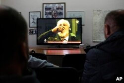FILE - Bosnians watch a live TV broadcast from the International Criminal Court for the former Yugoslavia (ICTY) in The Hague as Slobodan Praljak drinks from a bottle that was later confirmed to have contained poison, in southern Bosnian town of Mostar 140 kms south of Sarajevo, Nov. 29, 2017.