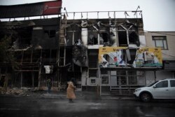 In a photo taken Nov. 18, 2019, and released by the Iranian Students' News Agency, ISNA, people walk past buildings which burned during protests that followed the authorities' decision to raise gasoline prices, in the city of Karaj, west of Tehran.