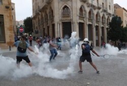 An anti-government protester uses a tennis racket to return a tear gas canister towards riot police during a protest near Parliament Square, in Beirut, Lebanon, Sept. 1, 2020.