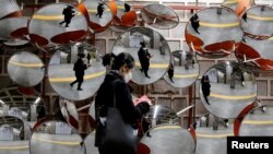 FILE - A woman wearing a mask to prevent the coronavirus is reflected in the mirrors, in Seoul, South Korea, Feb. 24, 2020.