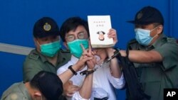 Pro-democracy activist Avery Ng, center, holds a book with a cover picture of Chinese President Xi Jinping as he is escorted by Correctional Services officers to a prison van for a court in Hong Kong, May 28, 2021. 