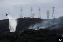 FILE - A helicopter drops water near power lines and electrical towers while working at a fire on San Bruno Mountain near Brisbane, California, Oct. 10, 2019.