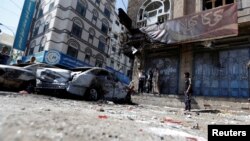 People stand next to damaged cars on a street where Houthi fighters recently clashed with forces loyal to Yemen's former president Ali Abdullah Saleh in Sanaa, Yemen Dec. 5, 2017.