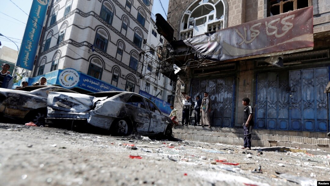 Orang-orang berdiri di samping mobil-mobil yang hancur pasca bentrokan pejuang Houthi dengan pasukan yang setia kepada mantan presiden Yaman Ali Abdullah Saleh baru-baru ini di Sanaa, Yaman, 5 Desember 2017.