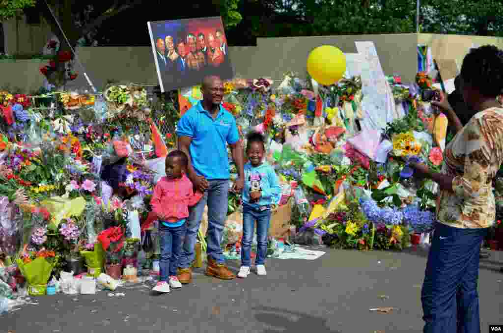 A family takes a photo in front of Nelson Mandela's home, where a makeshift memorial was set up in the street, Dec. 9, 2013. (Peter Cox for VOA) 