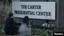 FILE - A woman holds flowers in front of a sign for The Carter Presidential Center after the death of former U.S. President Jimmy Carter at the age of 100 in Atlanta, Georgia, Dec. 29, 2024. 