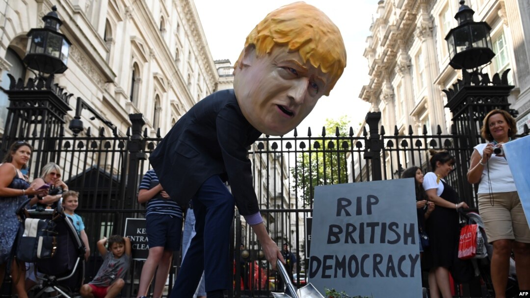 Sorang demonstran mengenakan topeng PM Boris Johnson dalam aksi demo di luar Downing Street di London, mengecam kebijakan Johnson, Rabu (28/8).