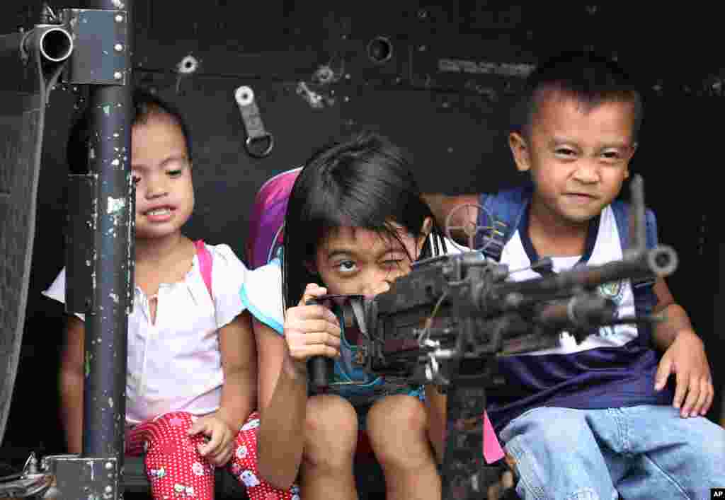 Anak-anak Filipina bermain dengan senjata di helikopter militer Filipina UH-1H dalam pameran untuk merayakan peringatan 75 tahun Departemen Pertahanan Nasional di pangkalan militer Kamp Aguinaldo di Quezon City, Filipina.