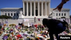 A woman places flowers as people mourn the death of Associate Justice Ruth Bader Ginsburg at the Supreme Court in Washington, Sept. 20, 2020. 