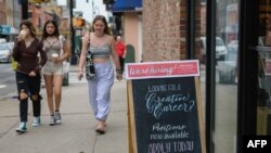 Un grupo de jóvenes pasa junto a un un cartel que reza "¡estamos contratando!" en una tienda en la ciudad de Nueva York, el 20 de agosto de 2021.