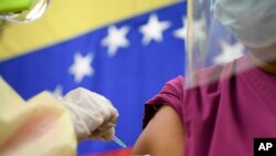 Con el telón de fondo de una bandera nacional, un médico inocula a un colega de trabajo con una dosis de la vacuna rusa COVID-19 Sputnik V en el hospital público Ana Francisca Pérez de León II en Caracas, Venezuela. Febrero 19, 2021. Foto: AP.