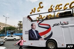 FILE - A school boy walks near an election campaign bus for Egypt's President Abdel Fattah al-Sisi adorned with his image, his slogan "long live Egypt," and C-shaped balloons, as Sisi's supporters prepare for a rally in Giza, the twin-city of the capital, on October 2, 2023.