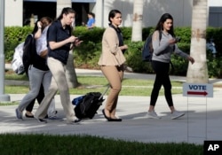 Students walk past a "Vote" sign next to an early voting site on the Florida International University campus, Oct. 23, 2018, in Miami.