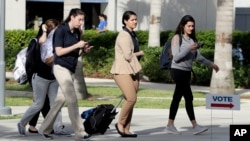 Students walk past a "Vote" sign next to an early voting site on the Florida International University campus, Oct. 23, 2018, in Miami. 