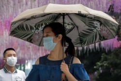 People wearing face masks to help curb the spread of the coronavirus walk by a decoration outside a shopping mall in Beijing, June 28, 2020.