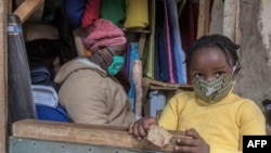 FILE - A woman who trades in fabrics, and her child, wears face masks as preventive measure against the COVID-19 coronavirus, in her shop inside Lilongwe City market in Lilongwe on May 18, 2020.