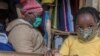 FILE - A woman who trades in fabrics, and her child, wears face masks as preventive measure against the COVID-19 coronavirus, in her shop inside Lilongwe City market in Lilongwe on May 18, 2020.