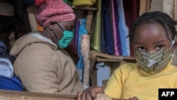 FILE - A woman who trades in fabrics, and her child, wears face masks as preventive measure against the COVID-19 coronavirus, in her shop inside Lilongwe City market in Lilongwe on May 18, 2020.