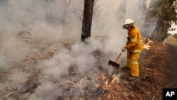 Seorang petugas pemadam kebakaran memindahkan puing-puing yang terbakar dalam upaya memadamkan api di dekat Burrill Lake, Australia, Minggu, 5 Januari 2020. (AP Photo / Rick Rycroft)