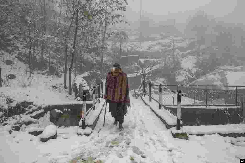 An elderly Kashmir villager walks on a snow covered road during the season&#39;s first snowfall on the outskirts of Srinagar, Indian-controlled Kashmir.