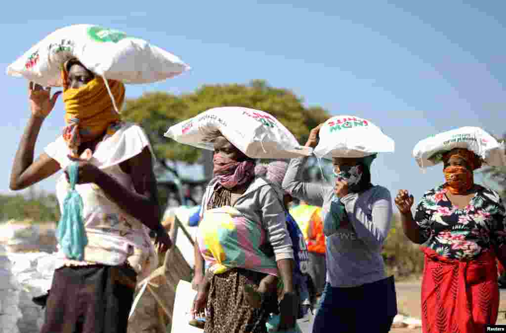 Mulheres carregam sacos de farinha de milho da ajuda alimentar num assentamento informal em Pret&#243;ria, &#193;frica do Sul.