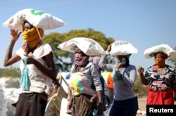 Para perempuan membawa karung berisi tepung jagung di atas kepala mereka saat antre menerima bantuan makanan di tengah pandemi COVID-19 di pemukiman informal Itireleng, dekat pinggiran kota Laudium di Pretoria, Afrika Selatan, 20 Mei 2020. (REUTERS/Siphiwe Sibeko)